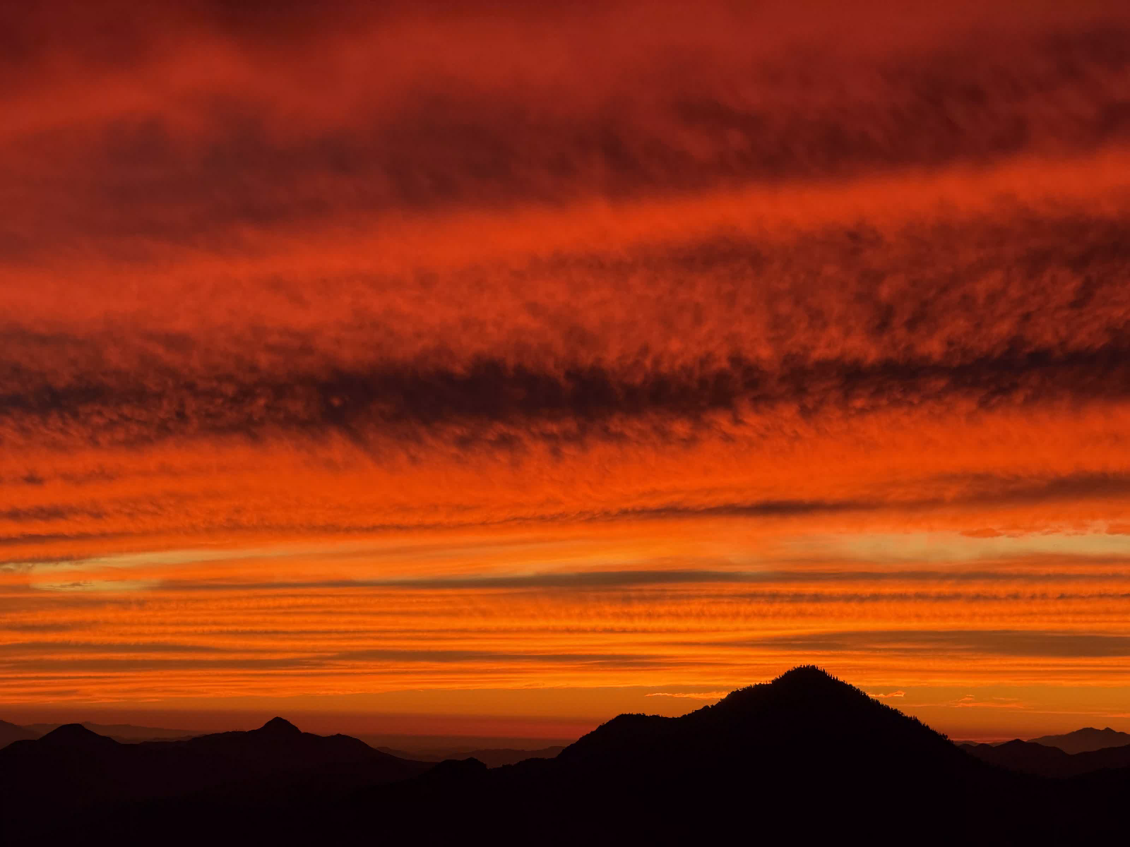 A sky of red and orange cloud bands over the dark silhouettes of the surrounding peaks at sunset